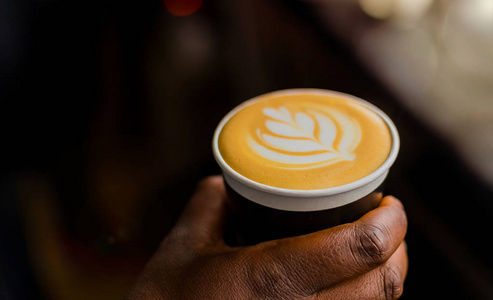 非洲咖啡咖啡师拿着一个带牛奶泡沫的叶子形状的外卖杯