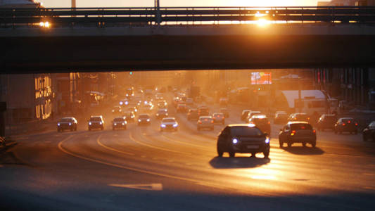 交通很拥挤。汽车在桥下的路上骑行。日落