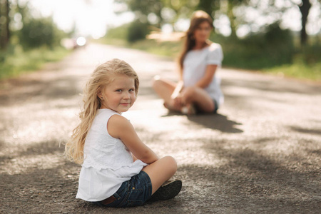 漂亮的妈妈和金发碧眼的女儿坐在马路附近的大胡同。他们微笑着看着 natune