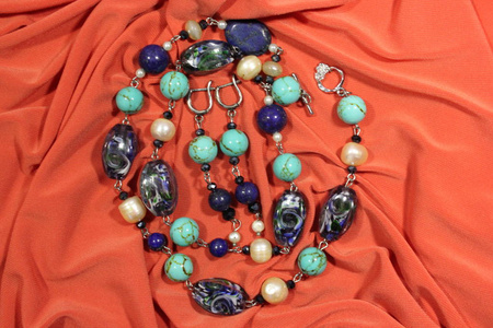 项链和耳环来自天然的半宝石蓝宝石和白色河流珍珠在粉红色的背景。 手工。