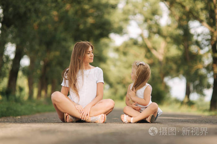 漂亮的妈妈和金发碧眼的女儿坐在马路附近的大胡同。他们微笑着看着 natune