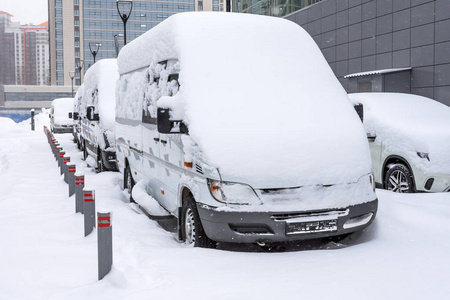 冬天在停车场的暴风雪中，白色的小型客车下雪了