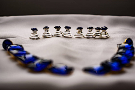 美丽时尚的女性珠宝和配饰。 白色纺织背景上有方形石头的蓝宝石耳环。 金色金属底座上蓝色明亮的莱茵石。 细高跟鞋小鹅卵石。