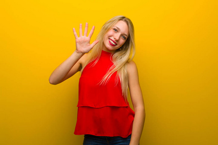 一个年轻的女孩穿着红色的衣服在黄色的墙上数着五个手指