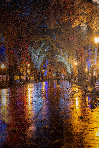模糊的夜景。 雨后夜晚城市的古老中心。 夜晚的城市街道，有明亮的彩灯的街道咖啡馆和移动的汽车。 运动模糊软焦点造型
