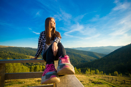 木台篱笆上留着长发的年轻女子欣赏美丽的山景