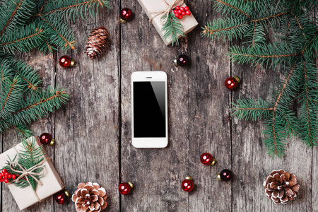 圣诞节背景与智能手机圣诞礼物冷杉枝在木制背景与冷杉枝。 圣诞节和新年快乐作文。 平躺式顶部视图