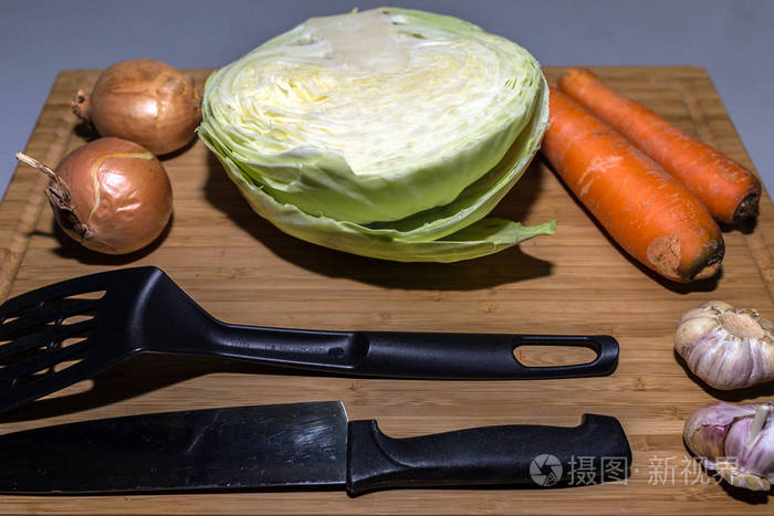 切板上的汤制品。 烹饪素食汤的新鲜食材。 卷心菜，胡萝卜，洋葱和大蒜在切割板上。