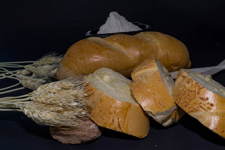 黑色背景上用穗子装饰的面包和小麦粉的静止生命