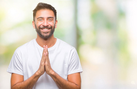 成年西班牙裔男子在孤立的背景下祈祷，双手一起祈求宽恕，微笑自信。