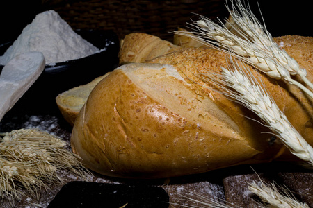 黑色背景上用穗子装饰的面包和小麦粉的静止生命