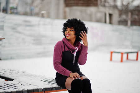 卷发非裔美国妇女在冬日坐在长凳上摆姿势。