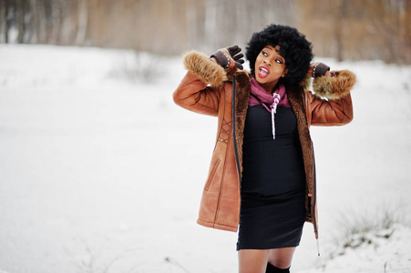 卷发非裔美国妇女穿着羊皮外套和手套在冬季摆姿势。