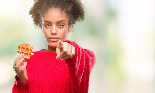 年轻美丽的非洲裔美国妇女吃华夫饼在孤立的背景上，手指指向相机和你的手标志积极和自信的手势从前面。