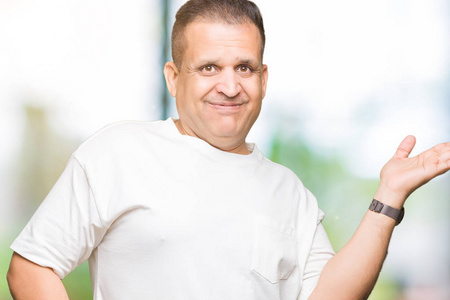 中年阿拉伯男人穿着白色T恤，在孤立的背景上微笑，欢快的呈现，用手掌指着相机。