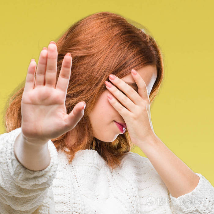 年轻的美女在孤立的背景上穿着冬天的毛衣,用手遮住眼睛,用悲伤和恐惧