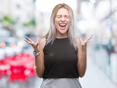 年轻的金发女人在孤立的背景下庆祝疯狂和疯狂的成功，举起手臂和闭上眼睛尖叫兴奋。 赢家概念