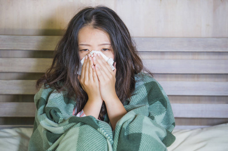 亚洲女性穿着被毯子覆盖的睡衣,患感冒和流感,在床上体温计,感到发烧