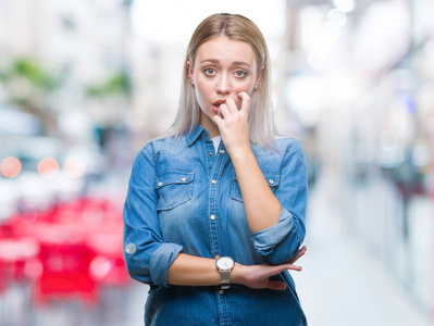 年轻的金发女人在孤立的背景上看起来压力和紧张，双手咬着嘴的指甲。 焦虑问题。