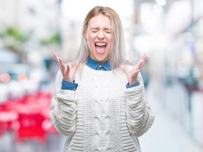 年轻的金发女人穿着冬天的毛衣，在孤立的背景上庆祝疯狂和疯狂的成功，手臂抬起和闭上的眼睛尖叫兴奋。 赢家概念