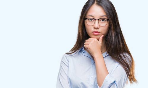 年轻的亚洲商务女性戴着眼镜，戴着孤立的背景，自信地看着相机，微笑着交叉的手臂和举起的手在下巴上。 积极思考。