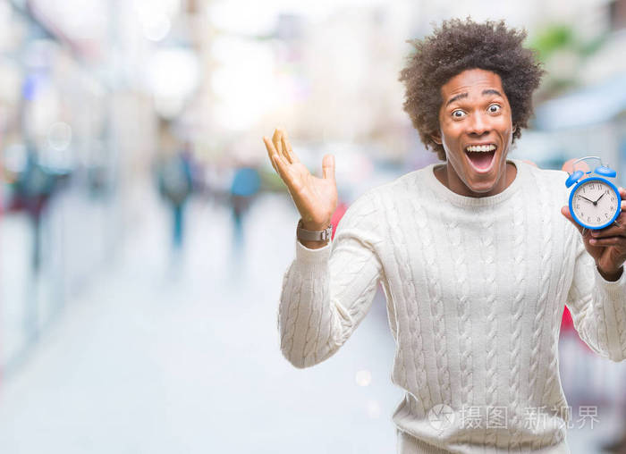 黑人男子拿着老式闹钟在孤立的背景下非常高兴和兴奋的胜利者表情庆祝