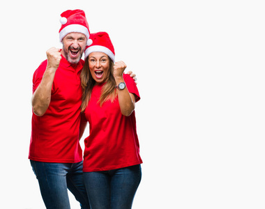 中年西班牙裔夫妇戴着圣诞帽，在孤立的背景下，非常高兴和兴奋地做着胜利者的手势，举起手臂，微笑着，尖叫着，争取成功。 庆祝概念。