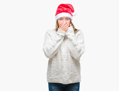 年轻美丽的高加索女人戴着圣诞帽，在孤立的背景下震惊地用手捂住嘴，因为错误。 秘密概念。