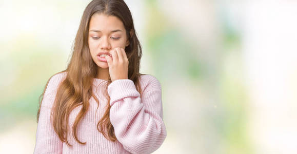 年轻漂亮的黑发女人穿着粉红色的冬季毛衣，在孤立的背景上看起来压力和紧张，双手咬着嘴的指甲。 焦虑问题。