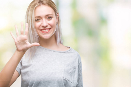 年轻的金发女子在孤立的背景显示和指着第五个手指，同时微笑自信和快乐。