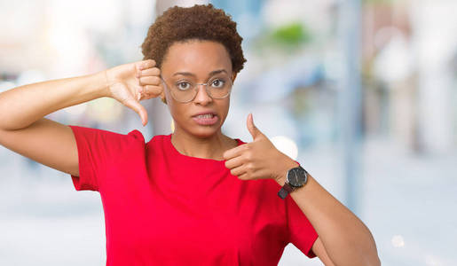 美丽的年轻非洲裔美国妇女戴着眼镜，在孤立的背景下做拇指上下的分歧和一致的表达。 疯狂冲突