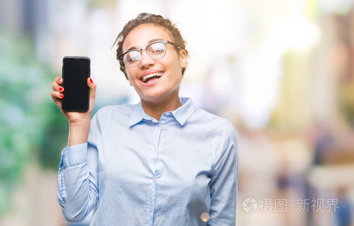 年轻的发非裔美国商业女孩展示智能手机屏幕上的孤立背景，快乐的脸站着，微笑着，自信的微笑，露出牙齿