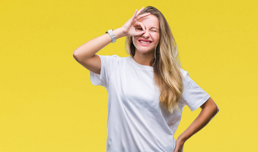年轻漂亮的金发女人穿着休闲的白色T恤，在孤立的背景上做着好的手势，用手微笑的眼睛透过手指看着幸福的脸。