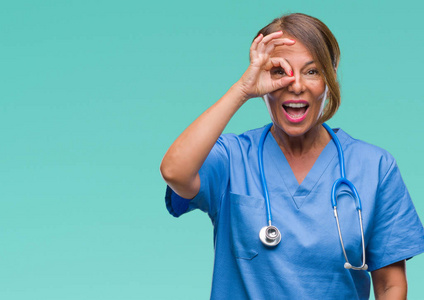 中年高级护士医生女士在孤立的背景下做OK手势，用手微笑的眼睛透过手指看着快乐的脸。