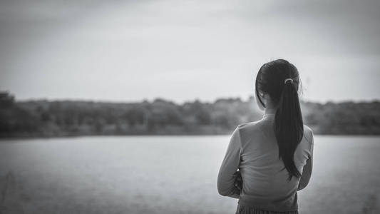 黑白孤独的女人独自站在河边。 孤独的悲伤概念。