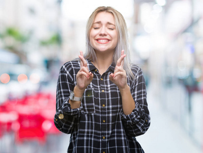 年轻的金发女人在孤立的背景上微笑着交叉手指与希望和眼睛闭上。 运气和迷信的概念。