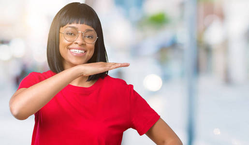 美丽的年轻非洲裔美国妇女戴着眼镜，在孤立的背景上做手势，用手显示大尺寸的标志符号。 微笑着看着相机。 测量概念。
