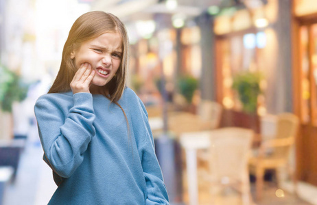 年轻漂亮的女孩穿着冬天的毛衣，在孤立的背景上摸着嘴，因为牙痛或牙齿上的牙齿疾病，用手痛苦地表达。 牙医的概念。