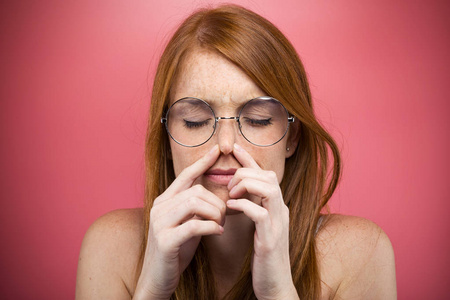 红头发的年轻女人在粉红色的背景上捏着她的鼻子。