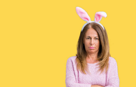 中年黑发妇女戴着复活节兔子耳朵，在孤立的背景怀疑和紧张的不赞成的表情在脸上交叉的手臂。 消极的人。