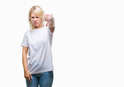 年轻漂亮的金发女人穿着白色T恤，在孤立的背景上看起来不高兴和愤怒，表现出拒绝和消极的拇指向下的手势。 不好的表情。