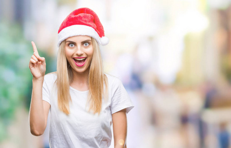 年轻漂亮的金发女人圣诞帽在孤立的背景上指着成功的想法。 退出并快乐。 一号。