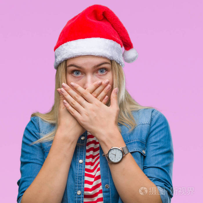 年轻的白种人女人戴着圣诞帽在孤立的背景下震惊地用手捂住嘴因为错误