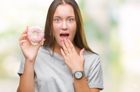 女人吃甜面包圈在孤立的背景上,用手捂住嘴,因错误而震惊,恐惧的表情
