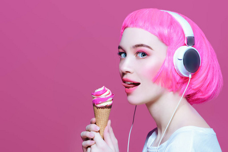 穿着耳机的粉红色头发的时髦女孩正在吃冰淇淋. 粉色背景.