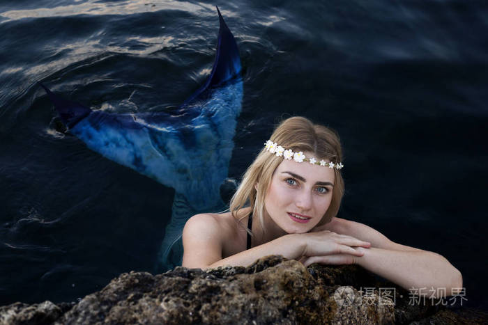 水中真正的美人鱼. 游到岸边. 躲在石头后面. 蓝色的尾巴.