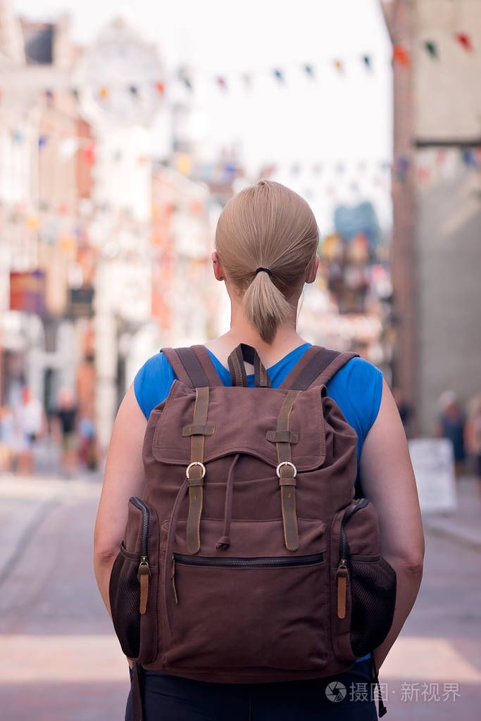 金发白种人女性站在英国一个小镇的大街上背着一个棕色的复古背包