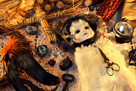 巫俗巫毒娃娃穿着新娘礼服,公鸡羽毛交叉,黑色蜡烛在花边餐巾纸上.