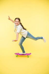 孩子有乐趣与便士板。爱好最喜欢的活动。孩子的笑脸站在滑板上。佩妮板可爱的五颜六色的滑板女孩。让我们骑行吧。女孩乘坐便士板黄色背景