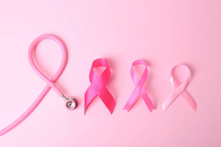 粉红色丝带与听诊器的颜色背景顶部视图。 乳腺癌概念